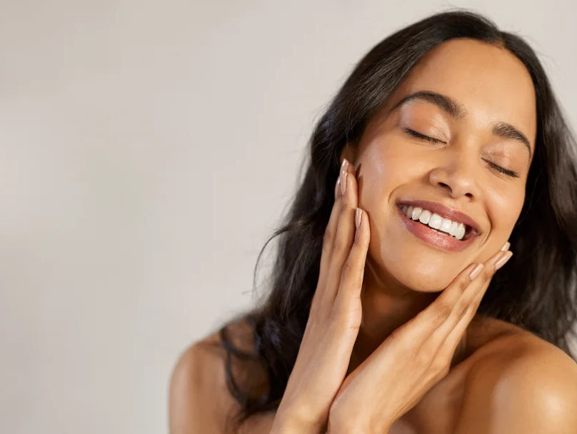 A woman smiling while gently touching her face, embodying a sense of joy and freshness after cleansing.