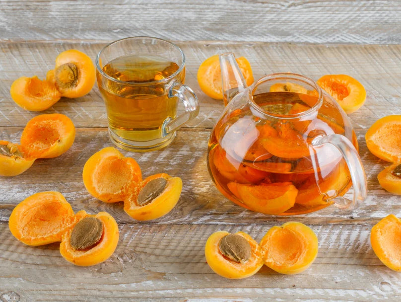 A glass pitcher of orange juice beside a bowl of sliced apricots, highlighting their use in skin-friendly apricot oil.