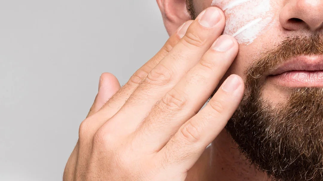 A man with a beard applies facial cream as part of his skincare routine.