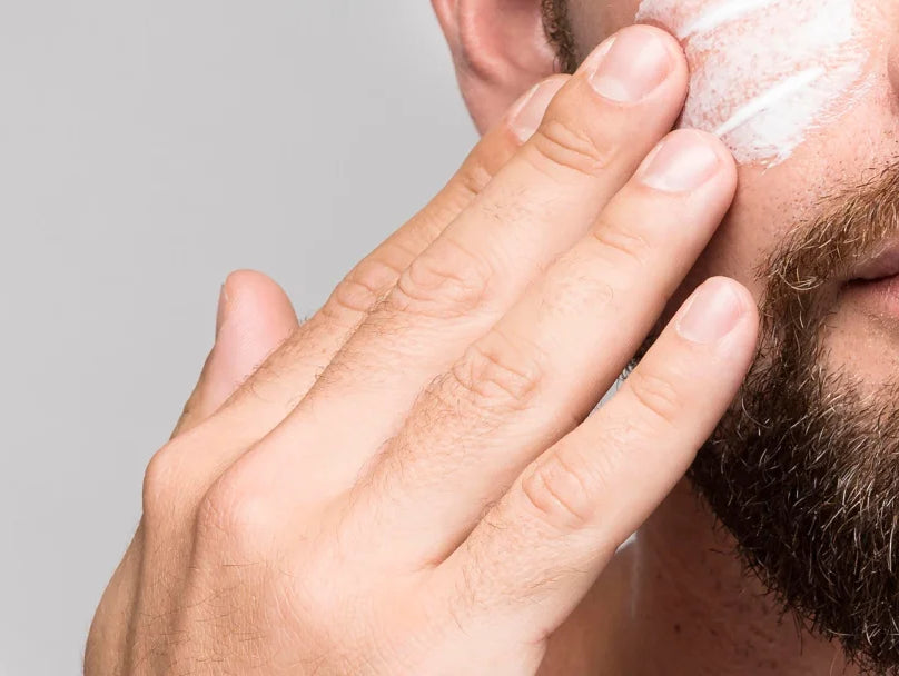 A man with a beard applies facial cream as part of his skincare routine.
