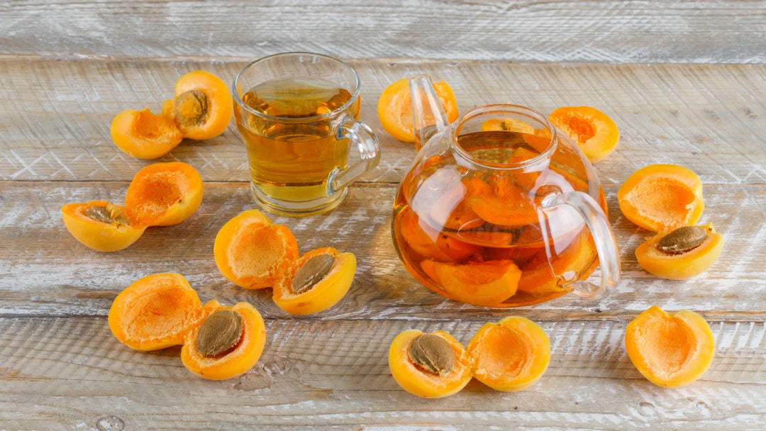 A glass pitcher of orange juice beside a bowl of sliced apricots, highlighting their use in skin-friendly apricot oil.